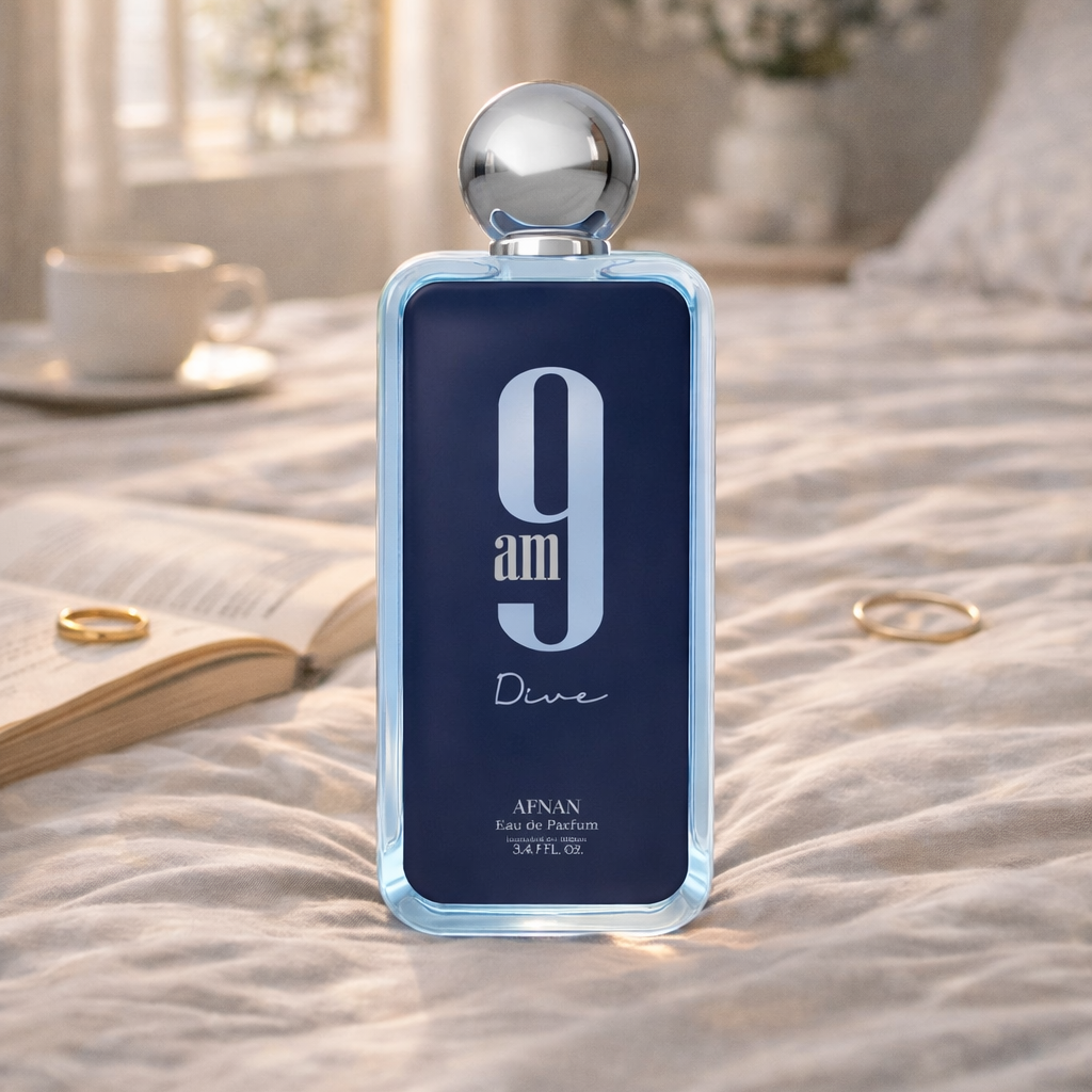 Perfume bottle labeled '9am Divine' by Afnan on a bed with a cup, book, and rings.