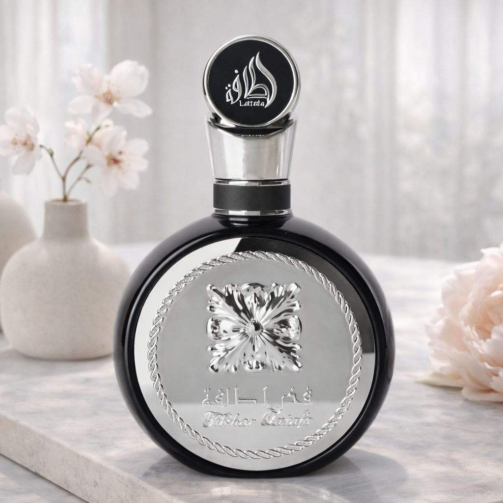 Black perfume bottle with silver cap and decorative elements on a light surface with flowers.